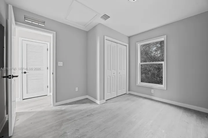 Interior space featuring neutral wall paint, wood-finish flooring, double-panel closet doors, and a single-hung window with exterior greenery