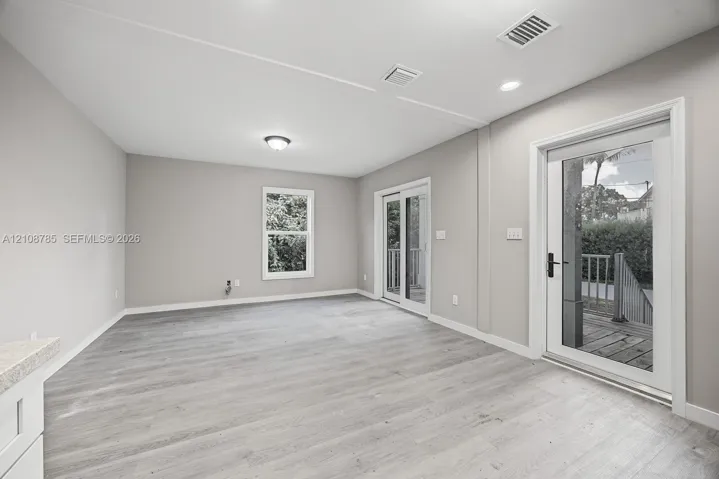 Neutral interior featuring wood-finish flooring, recessed lighting, double glass sliding doors, and a window with exterior greenery