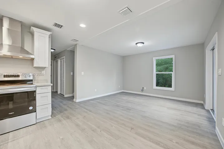 Kitchen featuring stainless steel range, professional-grade range hood, white cabinetry, and wood-finish flooring