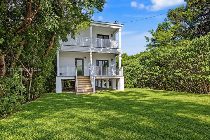 Two-story home with white horizontal siding, elevated foundation, stacked porches with metal railings, and exterior staircase