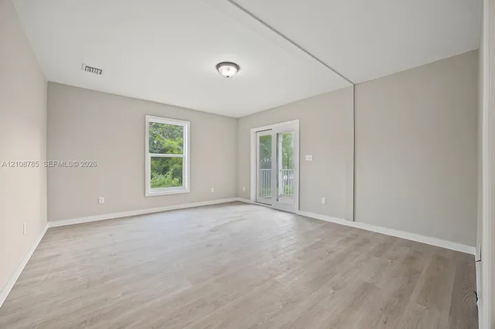 Neutral-toned interior featuring wood-finish flooring, a glass-pane sliding door with exterior access, a single window, and a flush-mount ceiling light fixture