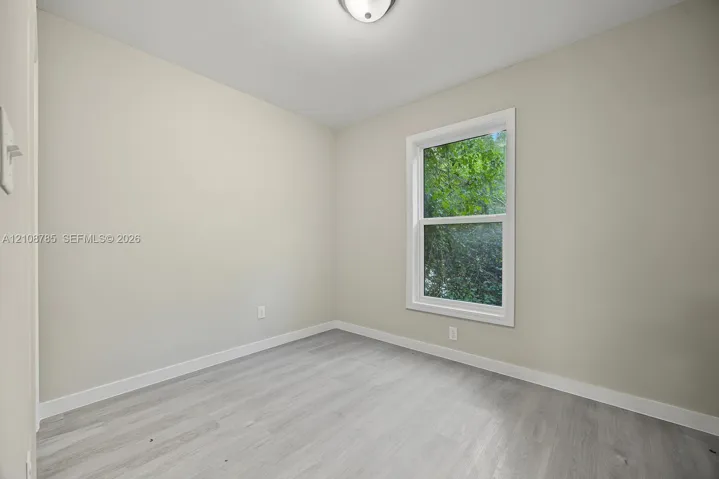 Neutral-toned walls, wood-finish flooring, and a double-hung window with a verdant exterior outlook, illuminated by a ceiling-mounted light fixture