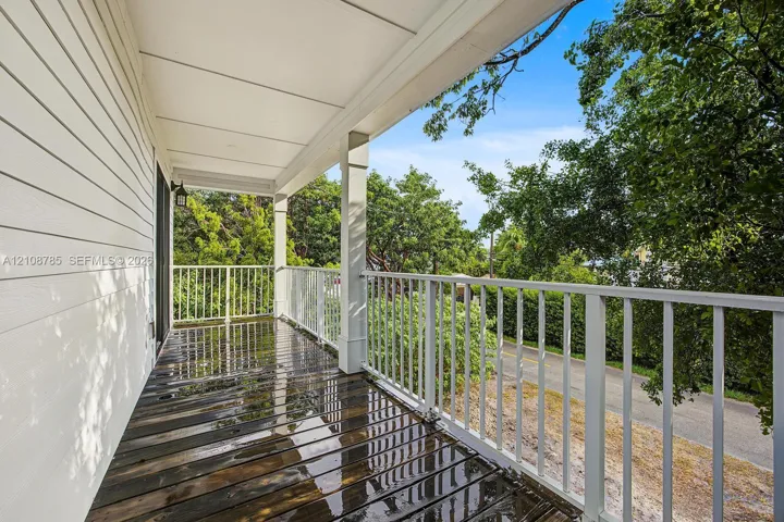 Covered exterior balcony featuring wood-plank flooring, white structural columns, and white vertical-bar railings