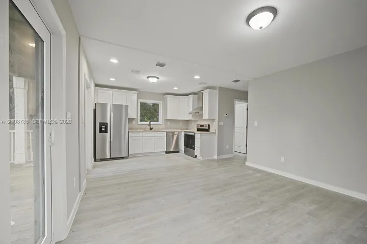 Kitchen featuring white cabinetry, stainless steel appliances, wood-finish flooring, recessed lighting, and a sliding glass door