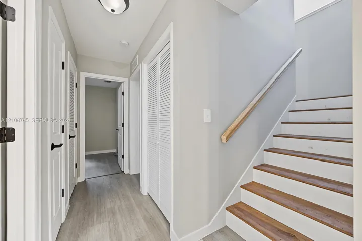 Staircase featuring wood-finish treads and a natural wood handrail, paired with interior doors showcasing matte black hardware and white louvered closet doors