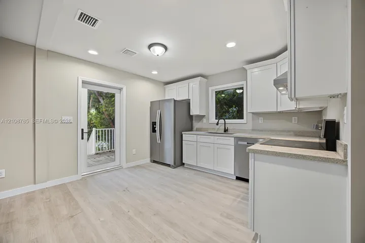 Kitchen featuring white cabinetry, stone-finish countertops, stainless steel appliances, a deep-basin sink with a matte black faucet, and wood-finish flooring