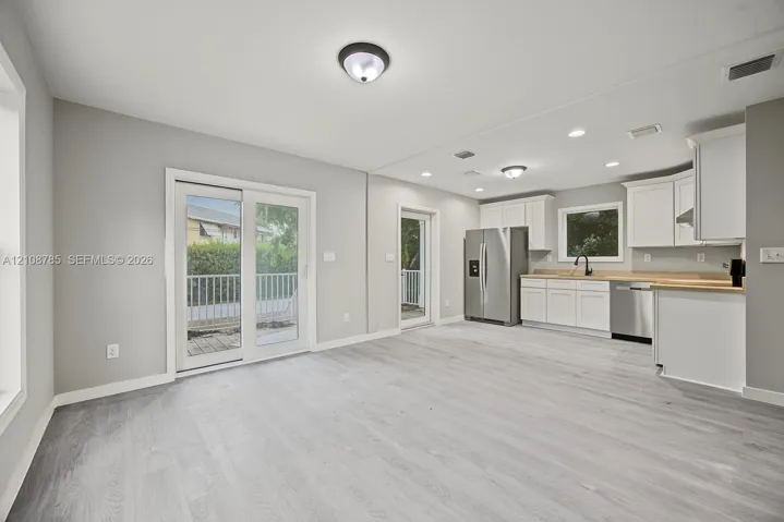 Open-concept space featuring wood-finish flooring, white shaker cabinetry, stainless steel appliances, neutral wall color, and glass sliding door access