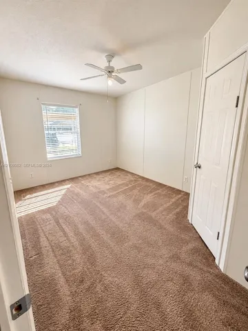Neutral-toned interior room featuring wall-to-wall carpeting, a multi-blade ceiling fan with integrated lighting, and a single-panel window with horizontal blinds