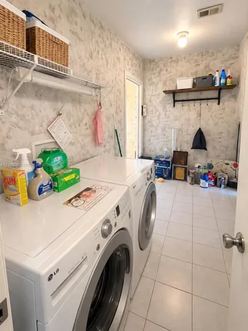 Laundry room featuring large-format tile flooring, textured wall finishes, wire shelving, and a wall-mounted wooden shelf with iron hardware