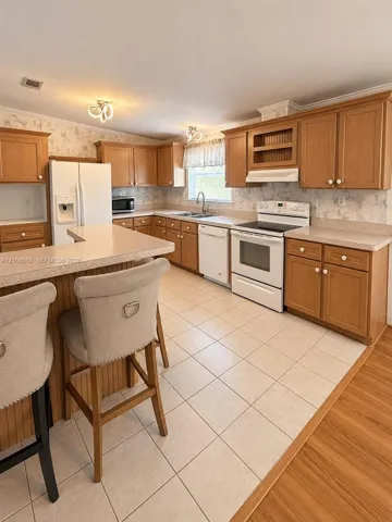 Kitchen featuring wood cabinetry, stone-texture laminate countertops, ceramic tile flooring, and integrated white appliances