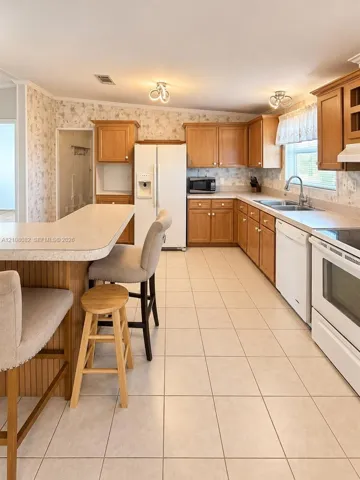 Kitchen featuring wood cabinetry, a breakfast bar, tile flooring, and white appliances