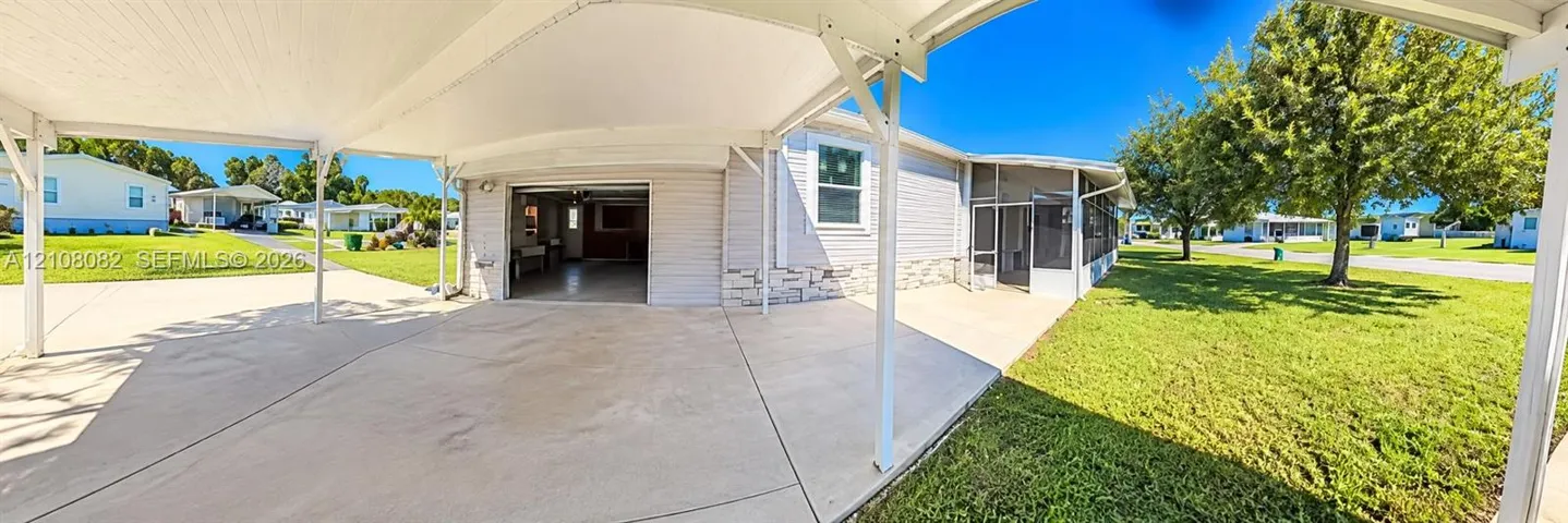 Covered carport with concrete flooring, stone-veneer exterior skirting, and screened-in enclosure