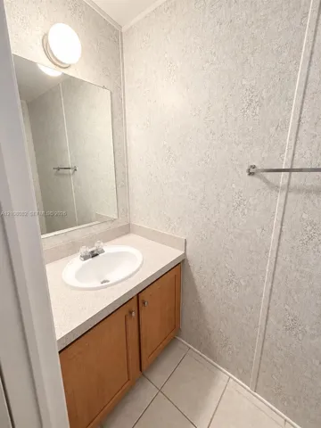 Vanity featuring a wood-finish cabinet, solid surface countertop with an integrated oval sink, wall-mounted mirror, overhead light fixture, and tile flooring