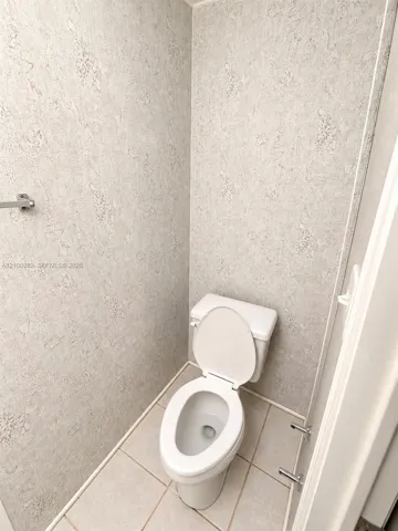 Restroom featuring neutral textured wall coverings, ceramic tile flooring, and a standard-height porcelain toilet