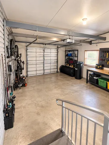 Attached garage featuring concrete flooring, structural steel beams, a metal sectional garage door, and a dedicated workspace area with an integrated wall-mounted tool board