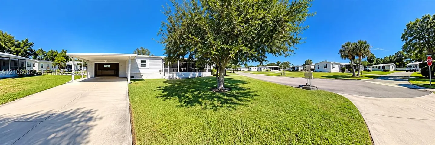 Exterior featuring a concrete driveway, attached carport, screened-in porch, and a lawn with mature trees