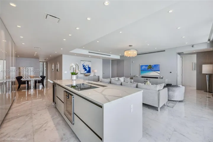 Open-concept interior featuring large-format stone flooring, recessed ceiling lighting, and a central kitchen island with integrated cooktop and built-in dishwasher