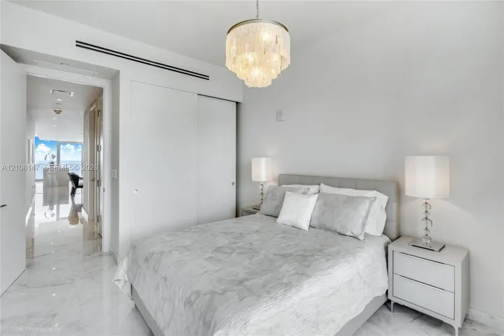 Multi-tiered crystal chandelier with a polished metal finish, polished stone-finish flooring, and built-in closet with sliding doors