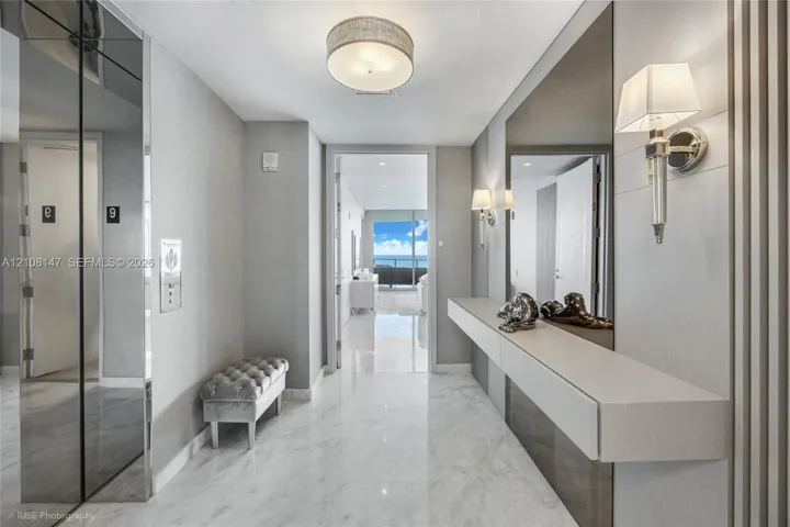 Foyer featuring polished stone flooring, custom wall-mounted floating console, mirrored wall panels, decorative wall sconces, and recessed drum ceiling lighting