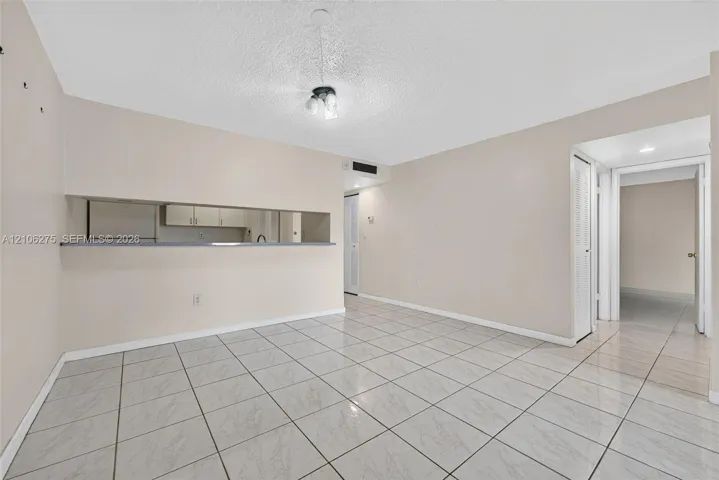 Open interior space featuring light-toned tile flooring, neutral wall paint, a pass-through opening to the kitchen, and a flush-mount ceiling fixture