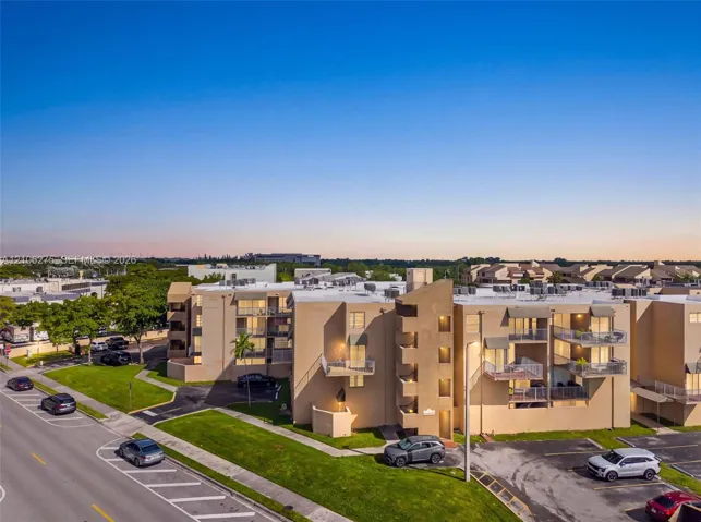 Multi-story residential complex featuring stucco exterior walls, private balconies with metal railings, and asphalt parking areas