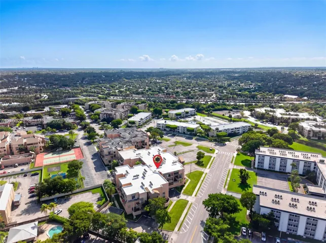 Aerial perspective of a multi-unit complex featuring flat roofing, paved surface parking, tennis courts, and a swimming pool