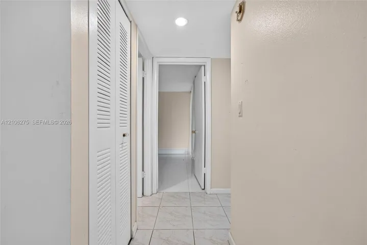 Hallway featuring white floor tiling, recessed lighting, and a white louvered closet door