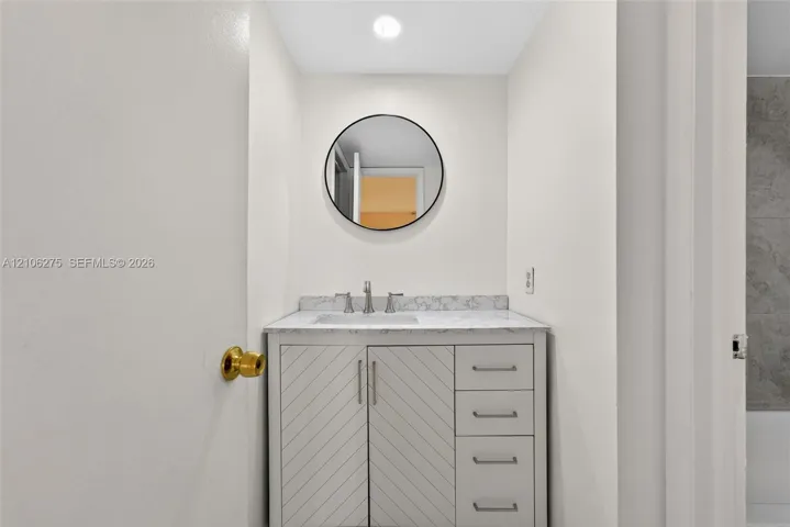 Vanity with stone-finish countertop, undermount sink, chevron-pattern cabinet doors, metallic hardware, and circular wall-mounted mirror