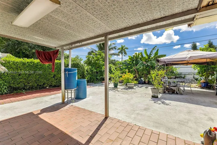 Covered patio area with brick-style paver flooring, concrete surface, and mature perimeter landscaping