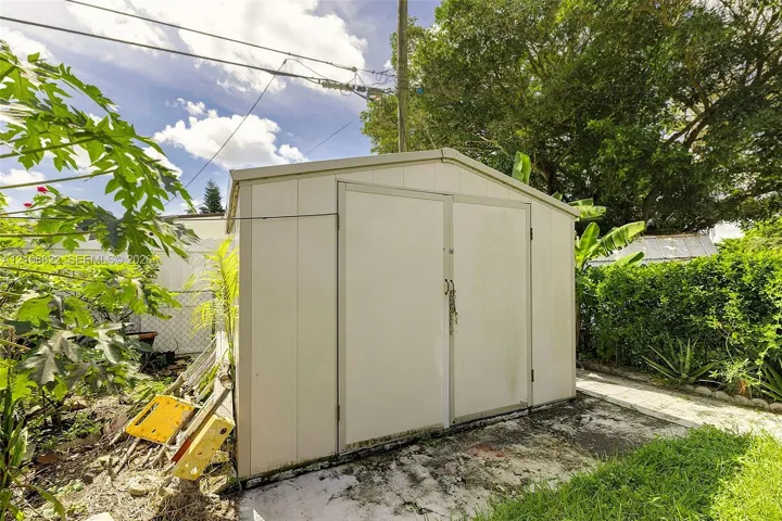 Detached metal storage structure featuring double doors and a gable roof, positioned on a concrete pad within the backyard