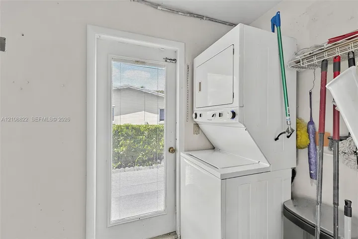 Stacked white laundry unit featuring front-loading controls and a full-lite exterior door with integrated blinds
