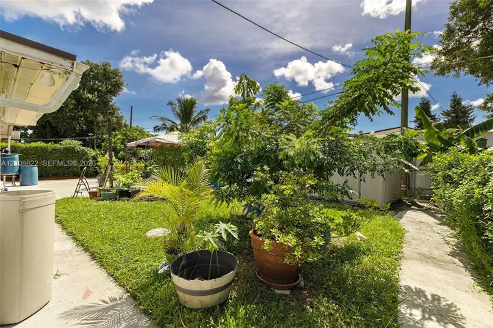 Outdoor space featuring a concrete patio, grassy lawn, mature greenery, and perimeter hedging