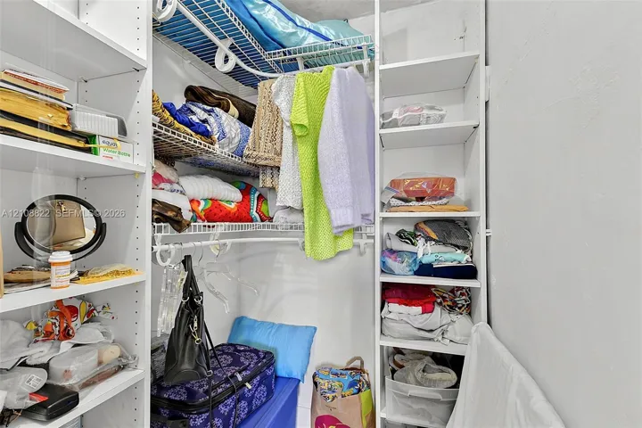 Walk-in closet featuring white built-in shelving and wire garment racks
