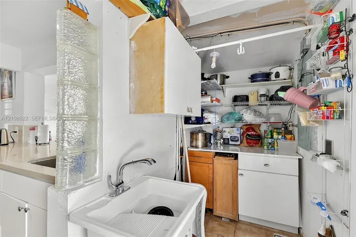Utility space featuring a glass block partition, a white deep-basin sink with a chrome faucet, built-in cabinetry, and open wire shelving