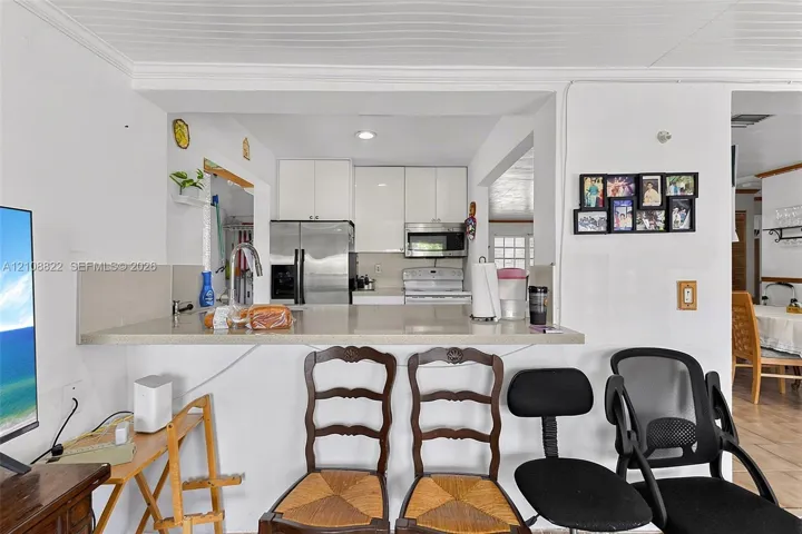 Kitchen featuring white cabinetry, a flat-surface countertop with an integrated bar, a stainless steel refrigerator, and a built-in microwave