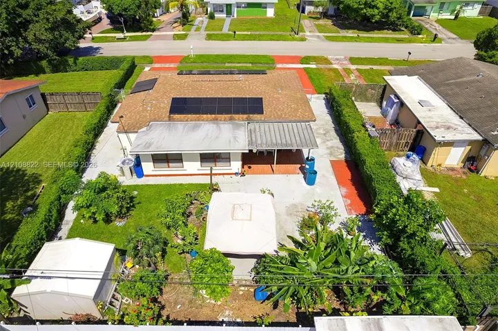 Exterior featuring a shingle roof equipped with solar panels, a covered patio, a concrete rear yard, and mature perimeter hedging