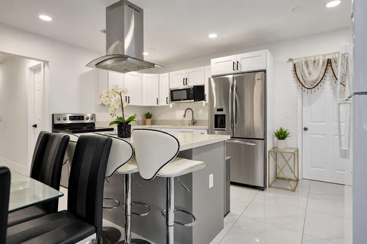 Kitchen featuring white shaker-style cabinetry, quartz countertops, stainless steel appliances, a stainless steel range hood, and tile flooring