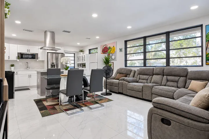Open-concept space featuring polished tile flooring, recessed lighting, white shaker-style cabinetry, stainless steel range hood, and large picture windows