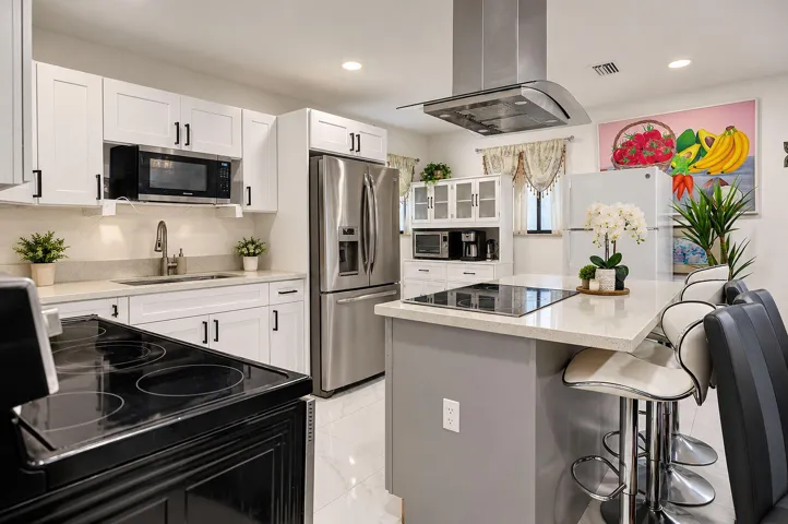 Kitchen featuring white shaker-style cabinetry, a central island with a stone-finish countertop, stainless steel appliances, a glass-panel overhead range hood, and tile flooring