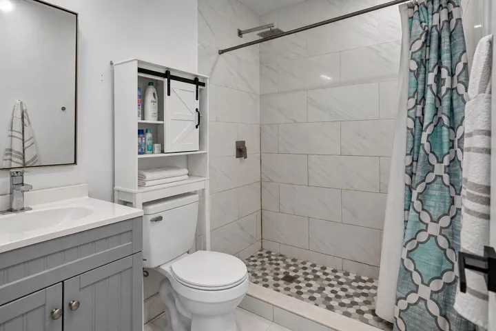 Grey shaker-style vanity with a solid surface countertop, rectangular under-mount sink, white subway-style shower wall tile, and geometric patterned shower floor tile