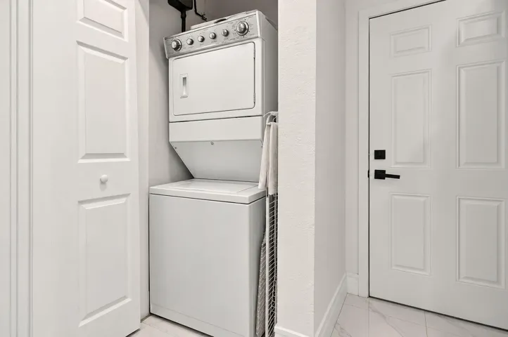 Laundry area featuring a stacked washer and dryer unit, four-panel interior doors, and tile flooring