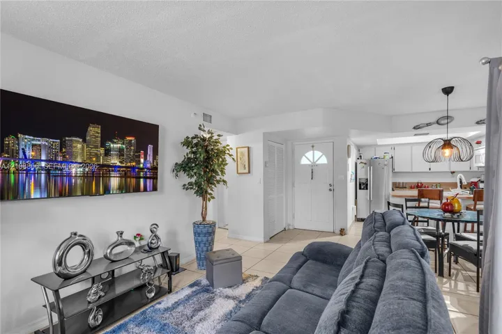 Open-concept area featuring neutral tile flooring, white cabinetry, a kitchen island, and a distinctive pendant light fixture