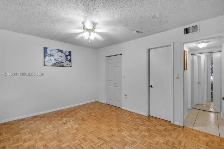 Parquet wood-finish flooring, white walls, built-in dual-panel closet doors, and a ceiling-mounted light fixture with a fan