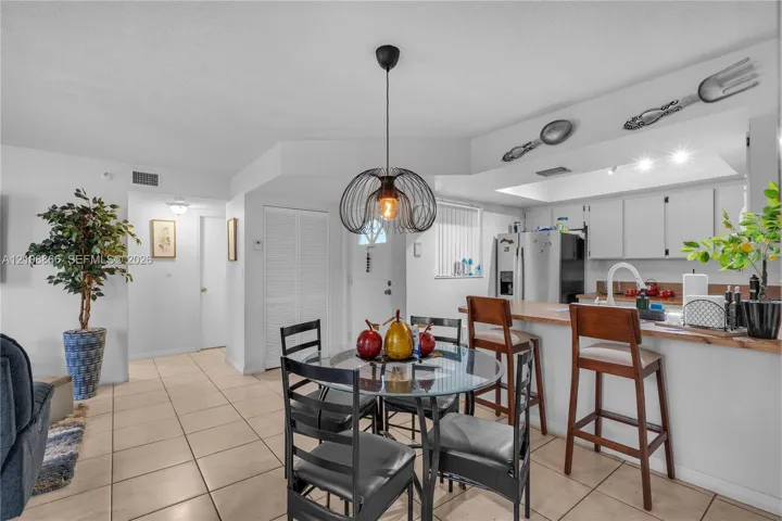 Open-concept kitchen featuring a breakfast bar with wood-finish countertop, white cabinetry, tile flooring, and a modern wire-frame pendant light