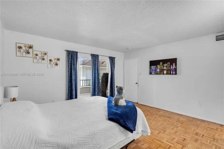 Interior space featuring wood-finish parquet flooring, textured ceiling, and a sliding glass door providing external access to a balcony with a railing