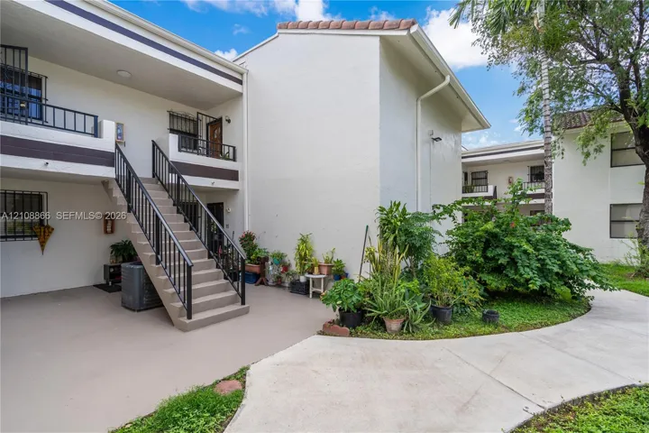 Stucco exterior with multi-level balconies, metal railings, exterior staircase, concrete walkways, and mature landscaping