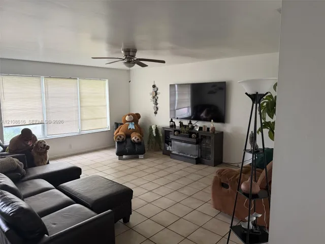 Living area featuring large windows with integrated blinds, square tile flooring, and a ceiling fan
