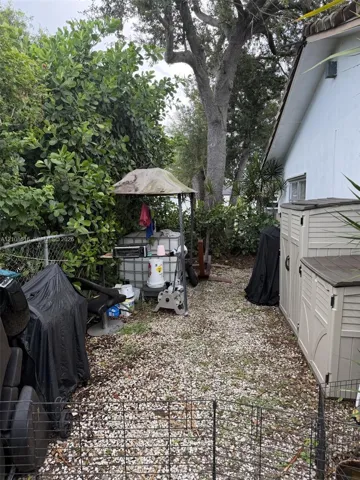 Side yard featuring a gravel ground surface, chain-link perimeter fencing, and mature trees