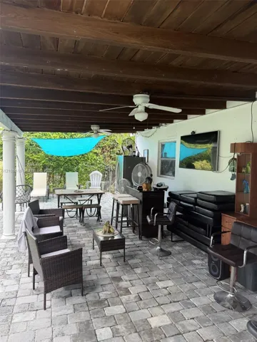 Covered patio featuring an exposed wood-beam ceiling, stone paver flooring, classic columns, and dual ceiling fans