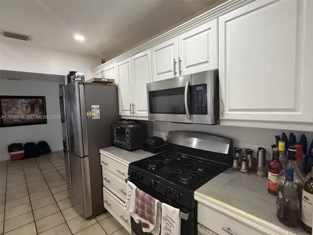 Kitchen featuring white shaker-style cabinetry with satin nickel hardware, stainless steel over-the-range microwave, stainless steel refrigerator, black gas range, and neutral tile flooring
